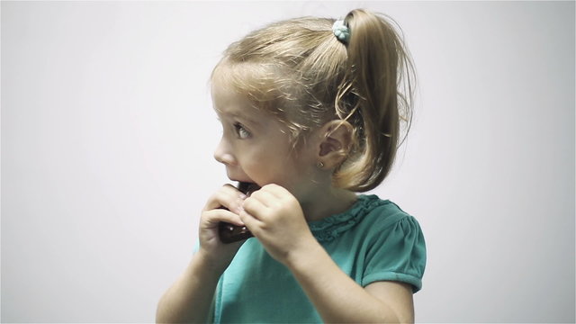 Little girl eating chocolate isolated on gray background