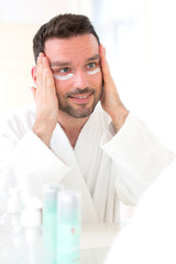 Young attractive man applying anti dark circles cream around eye
