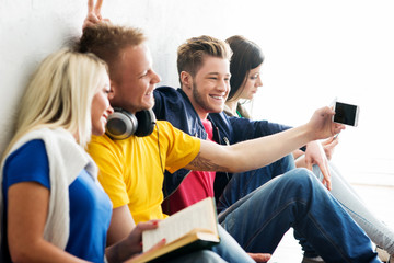 Group of happy students being on a break taking selfie. One of students is doing prank. Focus on a happy boy. Background is blurry.