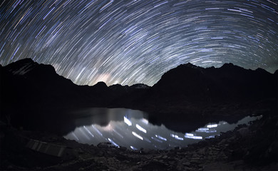 Star trails over the mountains and the reflection of the stars in a water beneath them.  - 90138569
