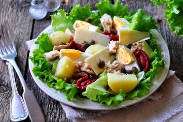 salad of lettuce, iceberg lettuce, with canned tuna, dried tomatoes, boiled potatoes, capers and parmesan cheese, dressed with olive oil. Selective focus. rustic style.