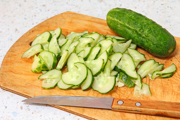 Cucumber and sliced segments on wooden cutting board.