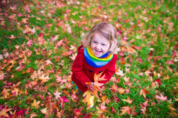 Little girl playing with maple leaf in autumn