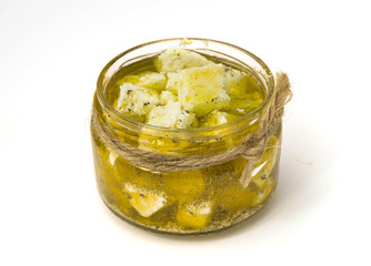 A jar of marinated Feta cheese in Olive oil and herbs, on white