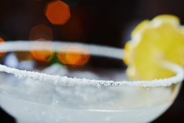 bright refreshing cocktail daiquiri on a table in a restaurant with creative decoration of orange slices and ice on a wooden table in a bar with a beautiful dance disco lights bokeh in the background.