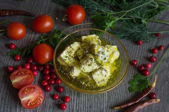 feta cheese in olive oil and herbs on a wooden table surrounded