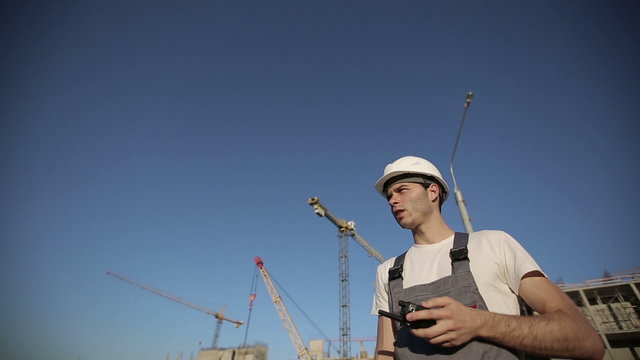 Engineer builder using a walkie talkie giving instructions at construction site. Long shot