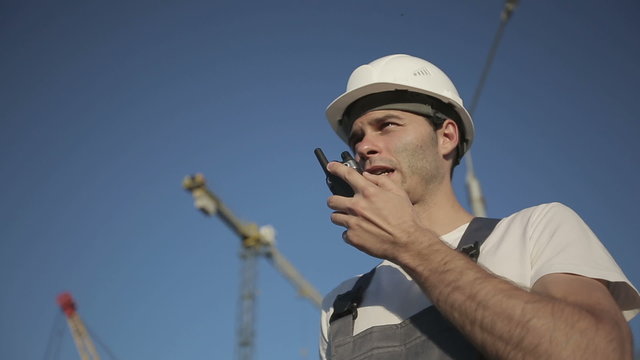 Engineer builder using a walkie talkie giving instructions at construction site. Medium shot