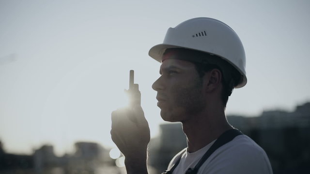 Engineer builder using a walkie talkie giving instructions at a construction site. Sunset time