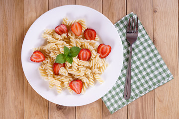 Pasta with strawberries on a plate on the oak table. Napkin with a fork. Top view.