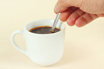 Hand mixing with a spoon of aromatic coffee in the cup