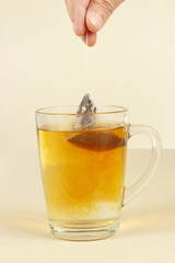 Hand brews tea bag in a glass of hot water