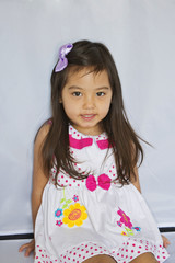 a toddler girl is sitting and smiling with a bright background.