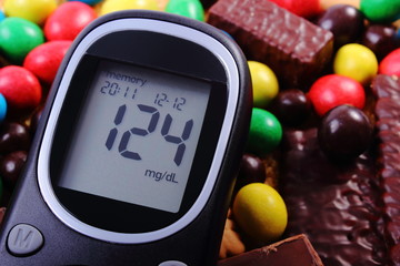Glucometer with heap of sweets and cane brown sugar, unhealthy food