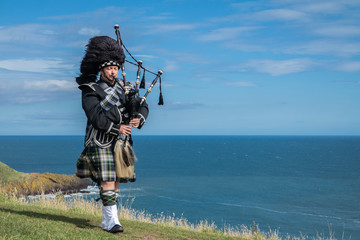 Traditional scottish bagpiper in full dress code with the sea in background - obrazy, fototapety, plakaty
