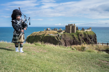 Traditional scottish bagpiper in full dress code at Dunnottar Castle in Stonehaven