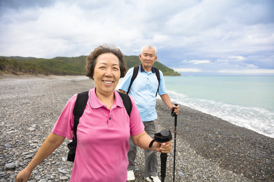 happy senior couple hiking on the coast beach