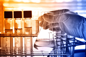 Flask in scientist hand with lab glassware background 