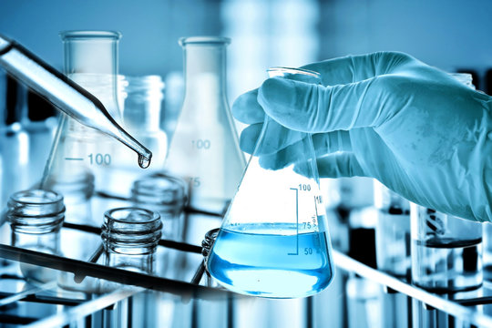 hand of scientist holding flask with lab glassware in chemical laboratory background, science laboratory research and development concept	