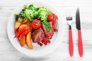 Tasty roasted meat with cranberry sauce and roasted vegetables on plate, on color wooden background