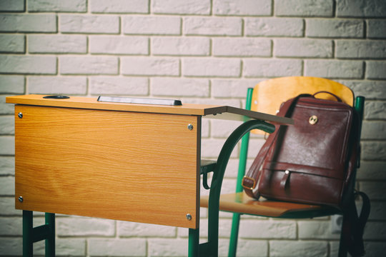 School desk and chair with bag on white brick wall background