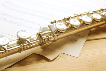 Obraz premium Silver flute with music notes on wooden table close up
