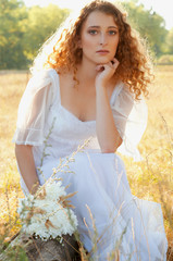 Fototapeta na wymiar Woman with curly golden hair sitting on a tree bark in summer fi