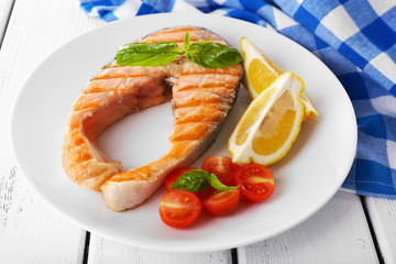 Tasty grilled salmon with tomato and lemon on table close up