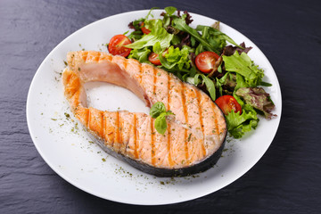 Tasty grilled salmon with salad on table close up