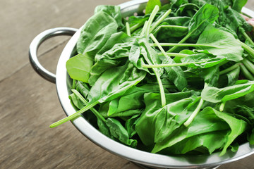 Fresh spinach leaves in colander on wooden table, closeup