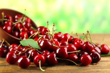 Pile of fresh cherries in bowl on wooden table on green blurred background