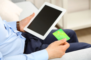 Man holding credit card and tablet on sofa in room