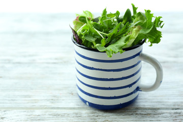 Fresh mixed green salad in cup on wooden table close up