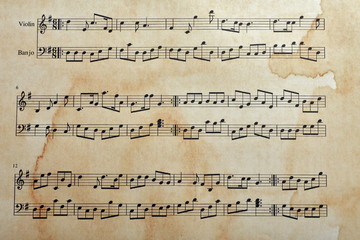Fototapeta premium Vintage sheet music for violin and banjo with aged paper texture and coffee stains, musical composition, the paper exhibits a textured surface with visible brown coffee stains