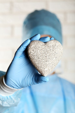 Doctor holding decorative stone heart on brick wall background