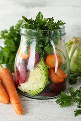Fresh vegetables in glass bottle on wooden table, closeup