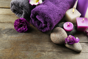 Obraz na płótnie Canvas Spa still life with towels, pebbles, purple flowers and candlelight on wooden table, closeup