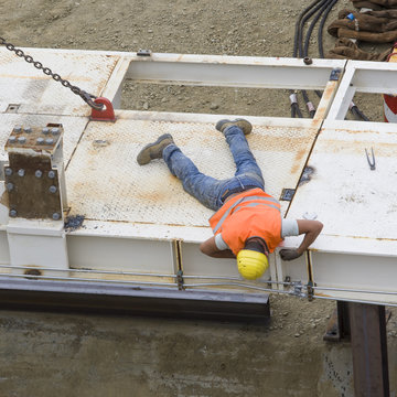 Operaio sdraiato in posizione prona sopra un ponte in costruzione 