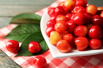 Sweet cherries with green leaves on plate, on wooden background