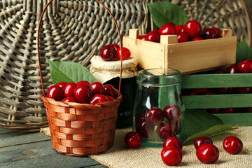 Fototapeta na wymiar Sweet cherries with green leaves in basket and wooden boxes, on wooden background