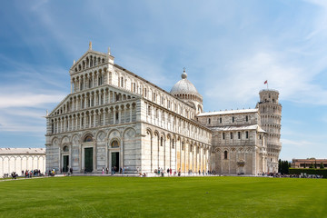 Beautiful view of the Cathedral and the Tower of Pisa. Italy. The Cathedral and the Tower are on the background of blue sky with light clouds. In the foreground a beautiful green lawn. Sunny day.