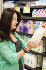 Woman in supermarket dressed in a green shirt and grey tanktop  is checking a bottle of milk