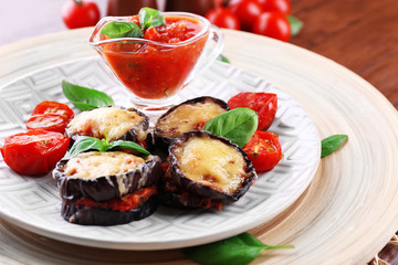 Dish of eggplant with cherry tomatoes and cheese in white plate on wooden table, closeup