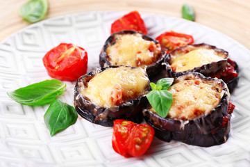 Dish of eggplant with cherry tomatoes and cheese in white plate on wooden table, closeup