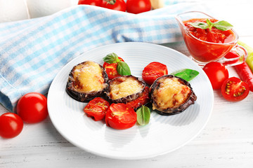 Dish of eggplant with cherry tomatoes and cheese in white plate on wooden table, closeup