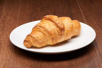 Fresh french croissant on white ceramic plate on dark wooden table background
