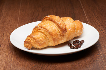 Fresh french croissant and coffee beans on white ceramic plate on dark wooden table background
