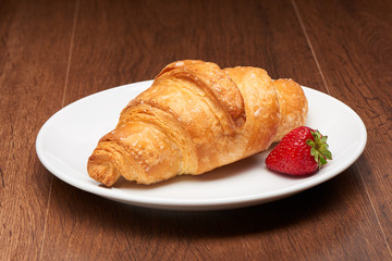 Fresh french croissant and strawberry on white ceramic plate on dark wooden table background