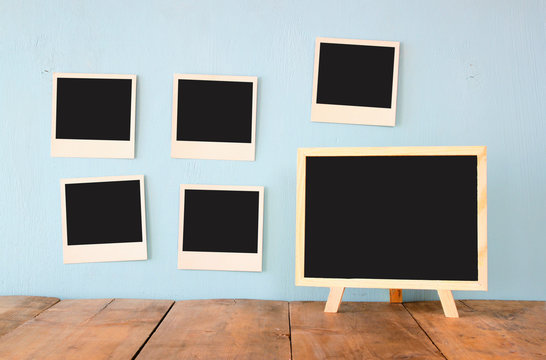 blank instant photos hang over wooden textured background next to blank blackboard
