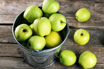 Ripe green apple in metal bucket on wooden table close up